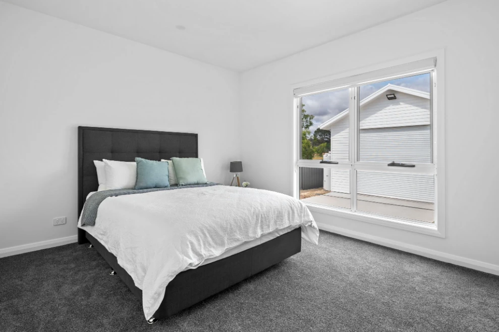 Modern bedroom with grey carpet and natural light.