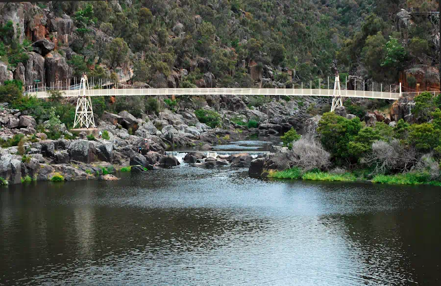 Suspension bridge over a tranquil river landscape.