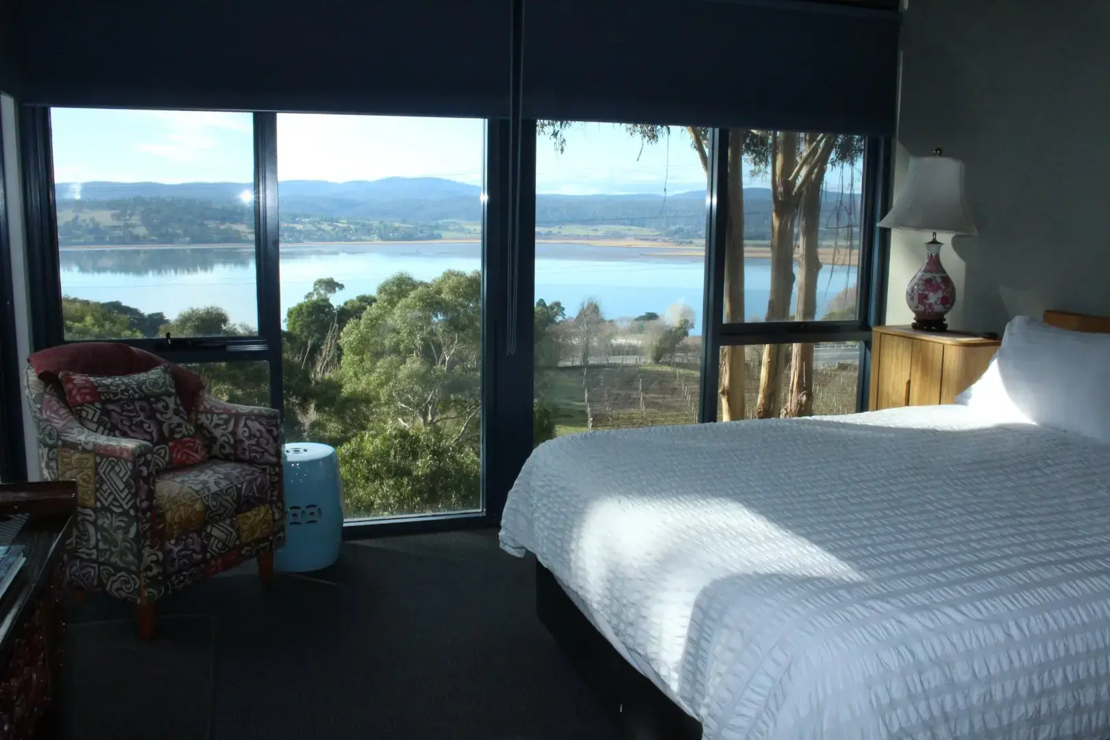 Bedroom with large windows overlooking lake and hills