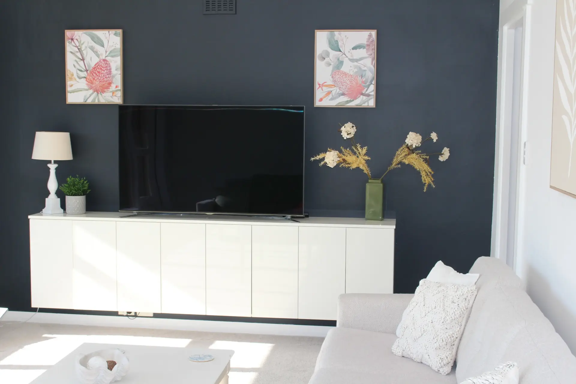 Modern living room with TV, plants, and artwork.