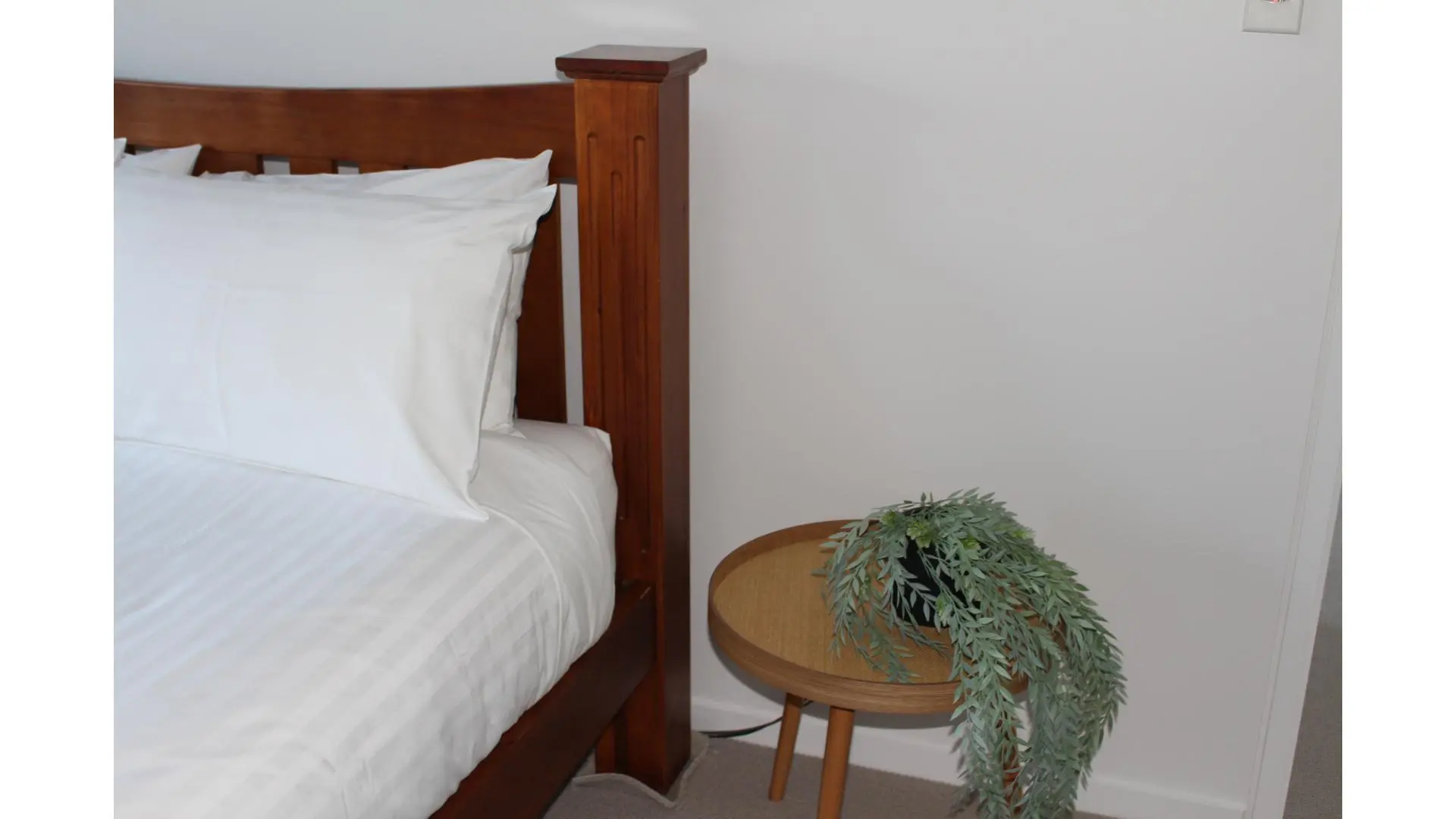 Bedside table with plant beside neatly made bed.