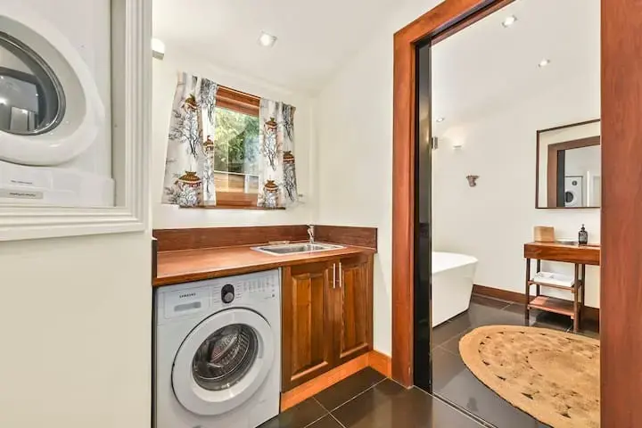 Laundry room leading to modern bathroom with bathtub