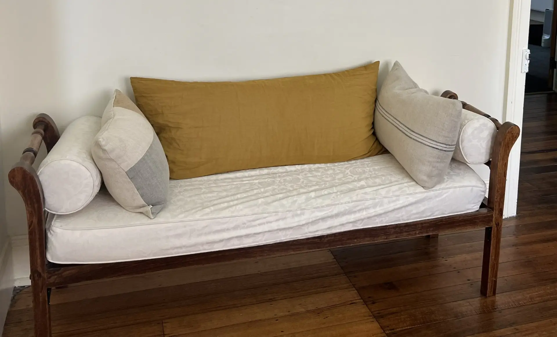 Wooden bench with white cushion and mustard pillow