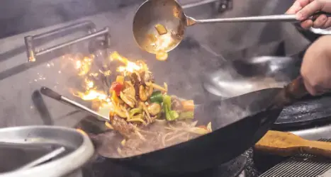 Chef stir-frying vegetables and meat in flaming wok